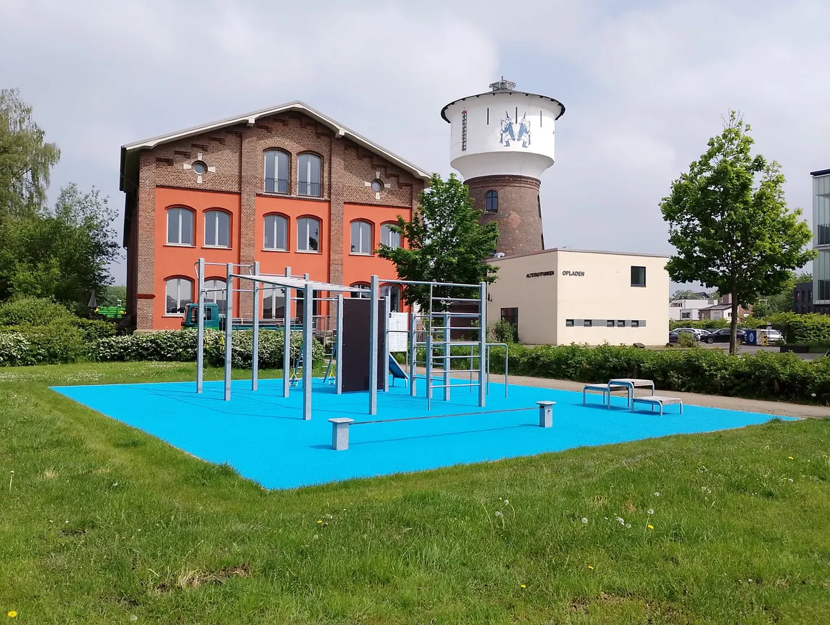 Bewegungsanlage mit blauem Fallschutzbelag und Randeinfassung vor einem Backsteingebäude