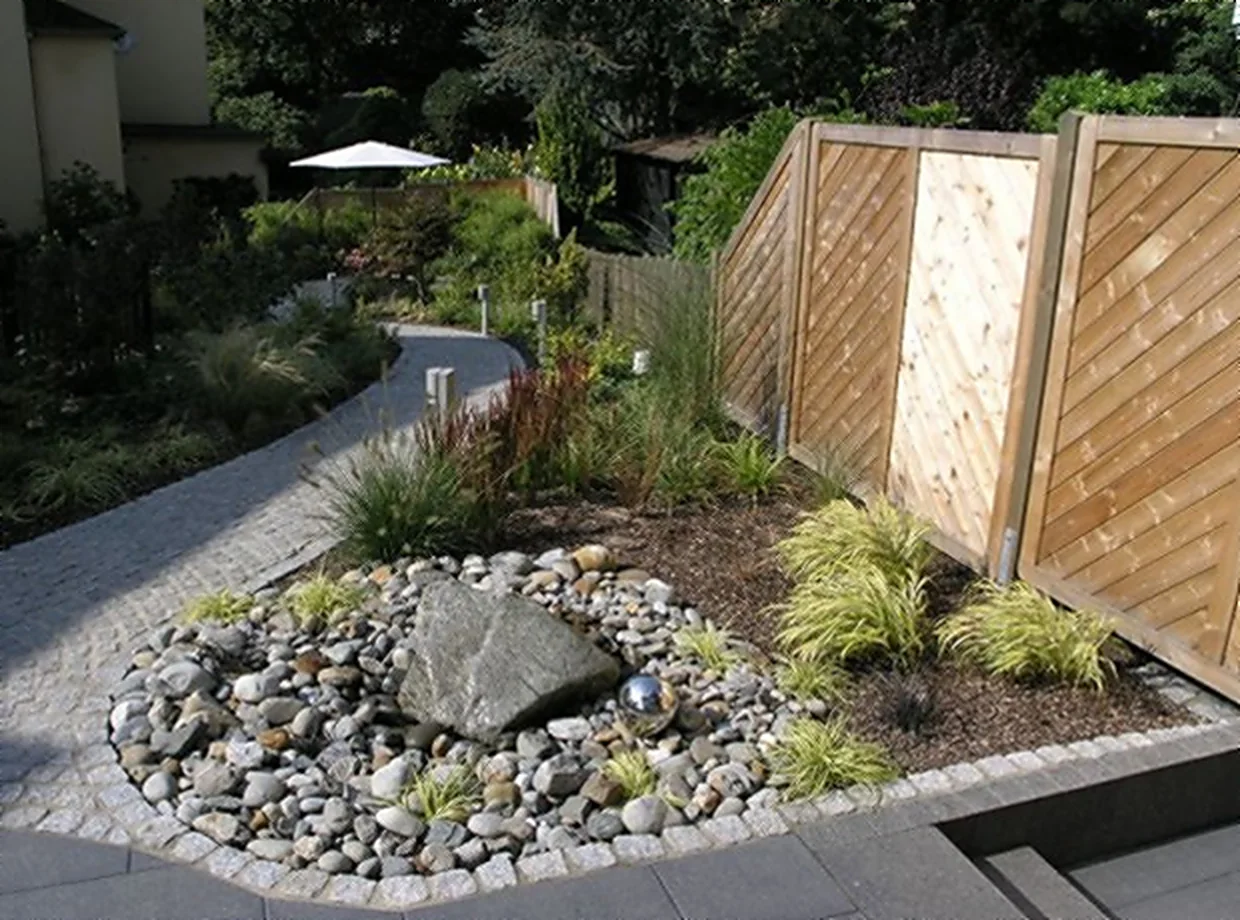 Neu gestalteter Hausgarten mit Holz-Sichtschutzwand, Kiesbeet mit Findling, Ziergräsern und geschwungenem Plattenweg