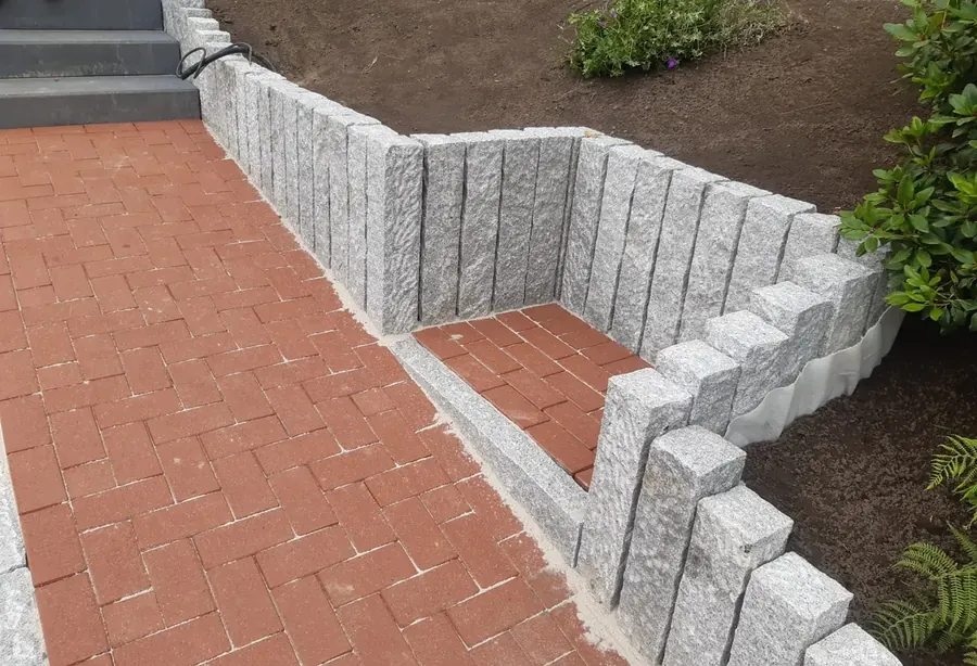 Stützmauer aus Granit-Winkelsteinen mit einer Stufe, davor eine Fläche aus rotem Klinkerpflaster