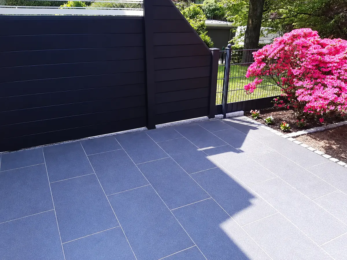 Terrasse aus großformatigen Betonwerksteinplatten mit anthrazitfarbener Sichtschutzwand und blühender Azalee